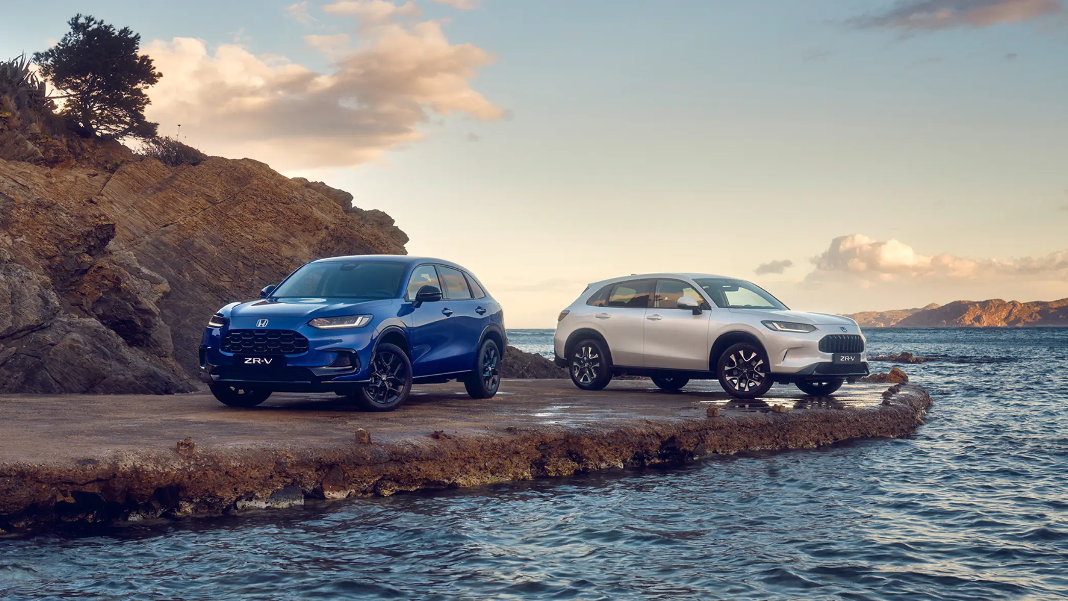 Trojštvrťový pohľad spredu na dve vozidlá ZR-V Hybrid zaparkované v horách.
