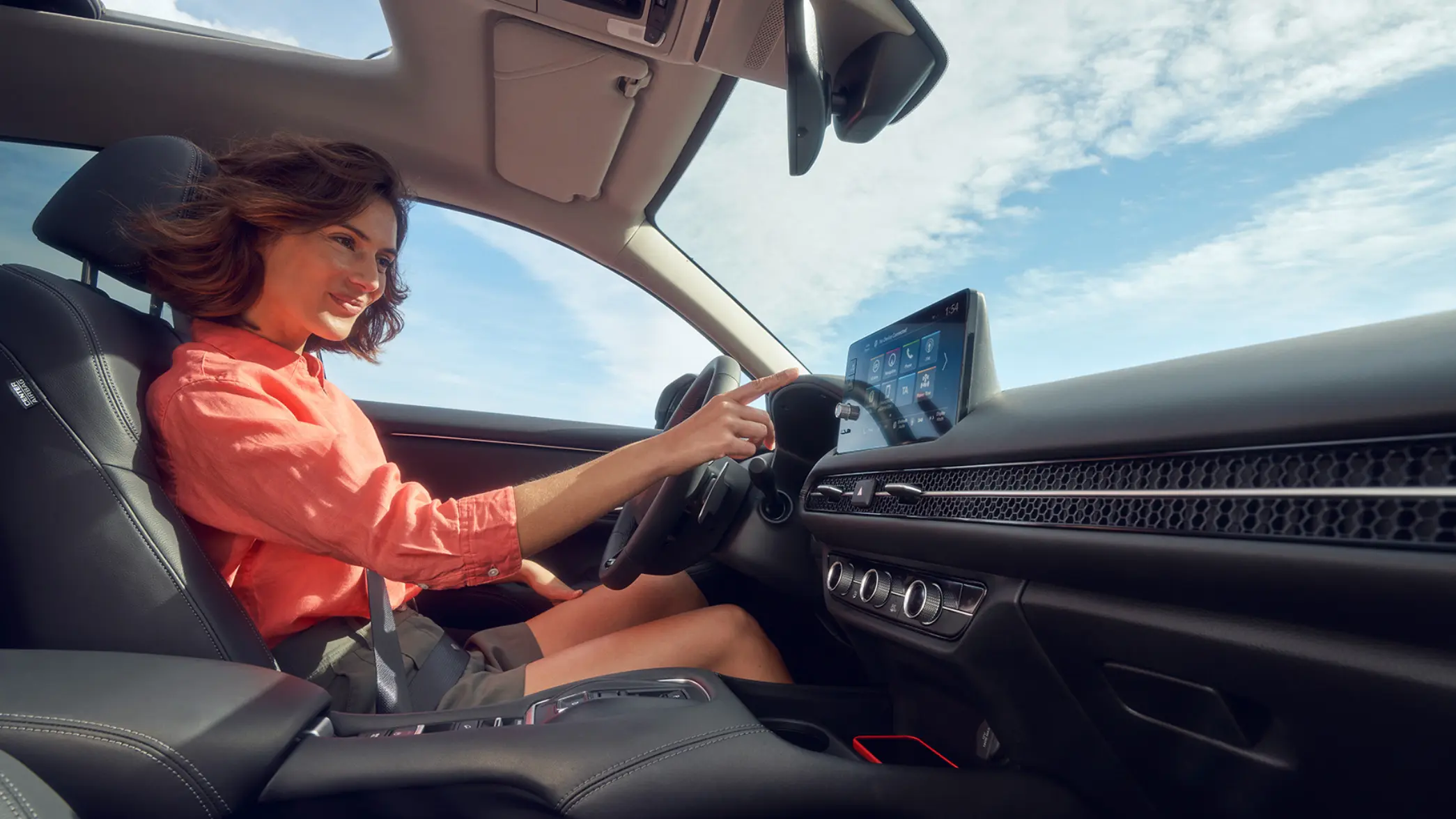 Žena sediaca na sedadle vodiča a ovládajúca obrazovku systému infotainment vozidla Honda ZR-V Hybrid.